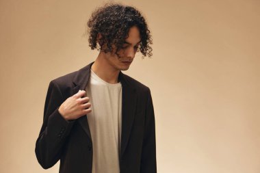 Klasik kahverengi ceketli, solaryum renginde harika kıvırcık bir adam bej renkli pastel arka planda yalnız poz veriyor. Yeni Moda Koleksiyonu teklifi. Retro stil konsepti. Reklam için boş yer