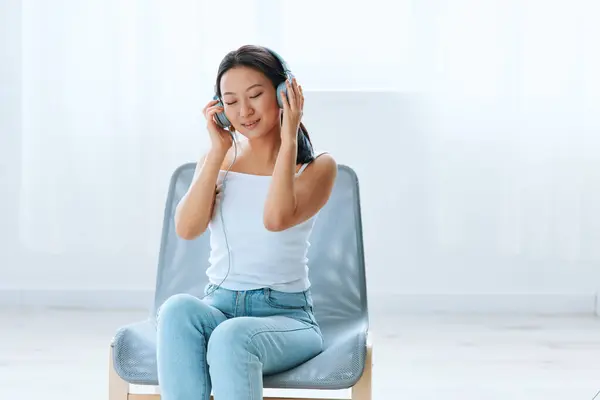 Enjoyed favorite playlist tanned lovely young Asian woman in headphones closing eyes relax at home interior living room. Sound Studio Stream, Social media concept. Cool offer Banner Wide angle