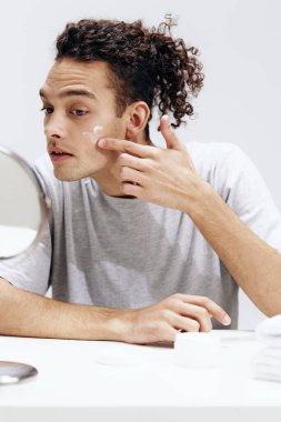 Yakışıklı adam yüzüne krem sürüyor ve aynadaki kozmetoloji yaşam tarzına bakıyor. Yüksek kalite fotoğraf