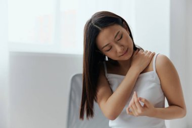 Omzu çıkmış, nevraljisi çıkmış, bronz tenli, genç bir Asyalı kadın evde oturma odasında omzuna dokunuyor. Yaralar Kötü Sağlık Hastalığı konsepti. Güzel teklif Banner.