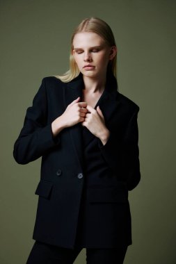 Model, stüdyoda yeşil bir arka planda poz verirken ceketi yakasından tutuyor. Kıyafet markaları için konsept fotoğraf. Şık takımlar için harika bir teklif. Yüksek kalite fotoğraf