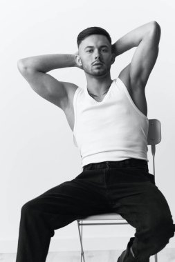 Fotoğrafları modelliyorum. Kendine güveni tam yakışıklı, yakışıklı, beyaz stüdyo arka planında oturan adam elini kaldırsın. Siyah ve Beyaz konsepti. Boşluğu kopyala