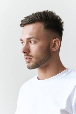 Temel tişörtlü yakışıklı, dalgın, ciddi, bronzlaşmış adamın portresi beyaz arka planda poz veriyor. Moda Tarzı Yeni Koleksiyon Teklifi. Reklam için boşluk kopyala. Model şıklatma