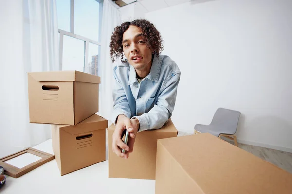guy with curly hair cardboard boxes in the room unpacking with phone Lifestyle. High quality photo