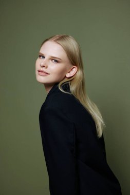 Çekici, güzel, zeki kız yeşil bir arka planda takım elbiseyle stüdyoda poz veren kameraya bakıyor. Yüksek kalite fotoğraf