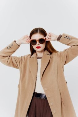 Dergi için reklam katalogu çekimi. Paltolu, gözlüklü, kızıl saçlı bir kız stüdyoda beyaz arka planda poz veriyor. Yüksek kalite fotoğraf