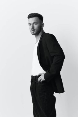 Fotoğrafları modelliyorum. Klasik takım elbiseli, narsist, çekici ve yakışıklı bir adam beyaz stüdyo arka planında izole bir şekilde duran kemerin üzerinde el ele tutuşuyor. Siyah beyaz kavramı. Moda teklifi. Boşluğu kopyala