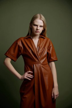 Markan için şık bir teklif. Modaya uygun sarışın kadın, el ele tutuşmuş deri yağmurluk giymiş, yeşil stüdyo arka planında izole edilmiş kameraya ciddi şekilde bakıyor.