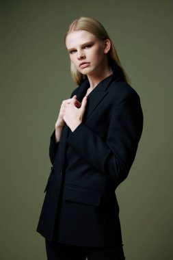 Sarışın güzel ceketini yakasından tutuyor. Stüdyoda yeşil bir arka planda yarım yamalak poz veriyor. Kıyafet markaları için konsept fotoğraf. Şık takımlar için harika bir teklif. Yüksek kalite fotoğraf