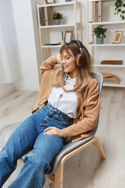 Enjoyed free time young blonde student lady freelancer in warm sweater in headphones listen fav songs sitting in armchair at modern home interior. Music time Relaxing Cool playlist Concept. Copy space