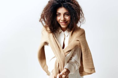 Kıvırcık Gülümseyen, Pastel Kazaklı Güzel Latin Kadın ve Beyaz Gömlekli, Beyaz Stüdyo Duvarı Arkaplanındaki İzole Edilmiş Kamera Pozisyonunda Ellerinizi Kaldırın. Moda Mevsimsel Satış Yeni Koleksiyon Kavramı.