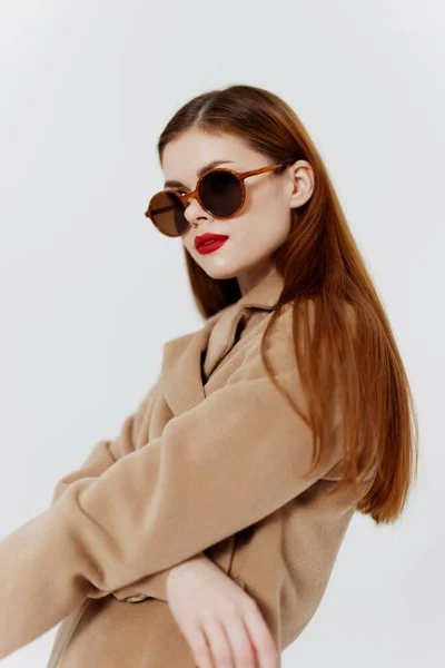 A red-haired professional model poses for a clothing brand magazine in a coat and glasses. High quality photo