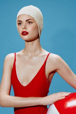 Yüzme şapkalı odaklanmış güzel bir bayan, mavi arka planda topu olan kırmızı bir mayo başka yere bakıyor. Kavramsal moda. Yüksek kalite fotoğraf