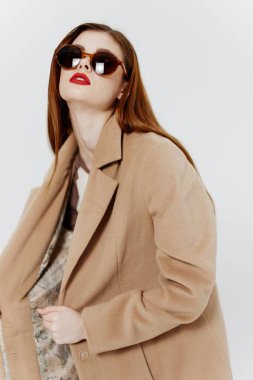 Palto giymiş baştan çıkarıcı bir kadın, stüdyonun beyaz arka planında bir giyim markasının reklamını yapıyor. Yüksek kalite fotoğraf