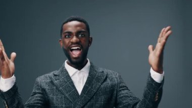 Genç bir Afro-Amerikalı adam kameraya bakmak için arkasını döner ve iş elbisesinin içinde güzel bir gülümsemeyle ellerini havada mutlu bir şekilde kaldırır. Yüksek kalite 4k görüntü
