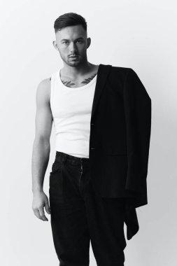 Fotoğrafları modelliyorum. Kendine güveni tam, ceketli yakışıklı bir adam beyaz stüdyo arka planında yalnız poz veriyor. Siyah ve Beyaz konsepti. Moda teklifi. Boşluğu kopyala