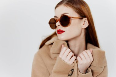 Palto mağazası için afiş. Gözlüklü genç kızıl saçlı bir kız stüdyoda beyaz bir arka planda ceket tasması tutuyor. Katalog fotoğrafçılığı. Yüksek kalite fotoğraf