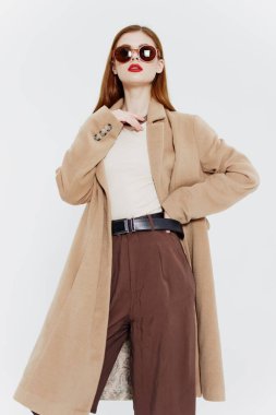 Kendine güveni tam kızıl saçlı, ceketli ve gözlüklü bir kız stüdyoda beyaz arka planda poz veriyor. Dergi için reklam katalogu çekimi. Yüksek kalite fotoğraf