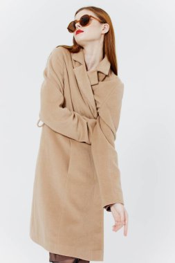 Kendine güveni tam kızıl saçlı, ceketli ve gözlüklü bir kız stüdyoda beyaz arka planda poz veriyor. Dergi için reklam katalogu çekimi. Yüksek kalite fotoğraf