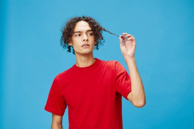 Düşünceli, düşünceli, mutsuz, bronzlaşmış, beyaz tenli, temel kırmızı tişörtlü adam mavi arka planda yalnız poz veriyor. Yaşam tarzı ve Duygular konsepti. Reklam için fotokopi alanı için iyi teklif.