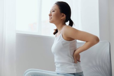 Uzun bir çalışmadan sonra skolyoz osteokondrozdan muzdarip olan genç Asyalı bir kadın koltuğa yanlış bir şekilde oturarak eklem ağrısı çekiyor. Yaralar Kötü Sağlık Hastalığı konsepti. Güzel teklif.