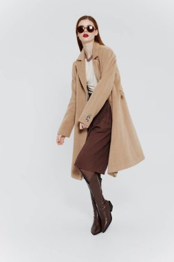 Stüdyoda beyaz bir arkaplanda poz veren bej gözlüklü kızıl saçlı şık bir bayan. Yüksek kalite fotoğraf