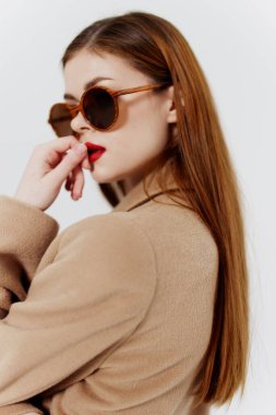 Gözlüklü ve bej ceketli şık bir genç kadın stüdyodaki bir katalog fotoğraf çekiminde beyaz bir arka planda poz veriyor. Yüksek kalite fotoğraf