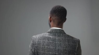 Genç bir Afro-Amerikalı adam kameraya bakmak için arkasını döner ve iş elbisesinin içinde güzel bir gülümsemeyle baş parmak işareti gösterir. Yüksek kalite 4k görüntü