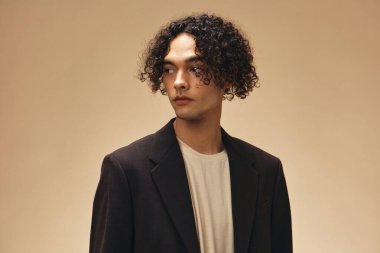 Klasik kahverengi ceketli, solaryum renginde harika kıvırcık bir adam bej renkli pastel arka planda yalnız poz veriyor. Yeni Moda Koleksiyonu teklifi. Retro stil konsepti. Reklam için boş yer