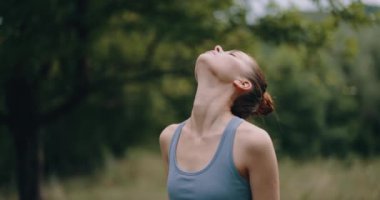 Parktaki bir kadın spor kıyafetleri içinde spor kıyafetleri ve doğa yaşam tarzıyla uyum içinde sırt ve bacak kaslarını esnetiyor ve pompalıyor. Yüksek kalite 4k görüntü