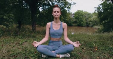 Nilüfer çiçeği pozunda meditasyon yapan bir kadın yazın yeşil çimenler üzerinde spor giyim parkında yoga yaparken. Yüksek kalite 4k görüntü