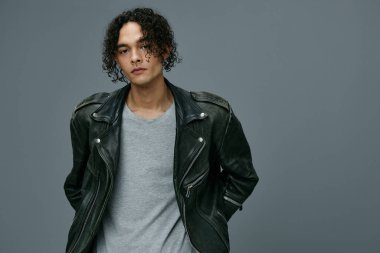 Kendine güvenen, bronz tenli, kıvırcık deri ceketli adam gri stüdyo arka planında izole edilmiş kameraya bakıyor. Güzel moda teklifi. Büyük Mevsimlik Satış Yeni Koleksiyon konsepti. İlan için alanı kopyala