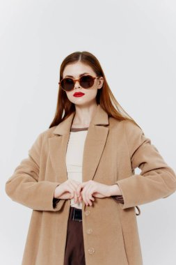 Dergi için reklam katalogu çekimi. Paltolu, gözlüklü, kızıl saçlı bir kız stüdyoda beyaz arka planda poz veriyor. Yüksek kalite fotoğraf