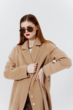 Dergi için reklam katalogu çekimi. Paltolu, gözlüklü, kızıl saçlı bir kız stüdyoda beyaz arka planda poz veriyor. Yüksek kalite fotoğraf