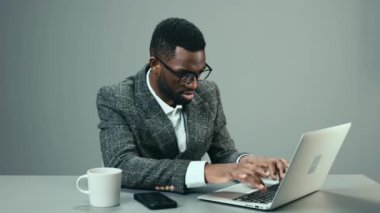 Ofiste çalışan Afro-Amerikalı bir işadamı masasında bir kupa kahveyle gri arka planda ve yorgun. Yüksek kalite 4k görüntü