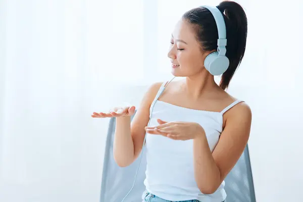 Relaxing dancing cheerful tanned lovely young Asian woman in headphones moves to music at home interior living room. Sound Studio Stream, Social media concept. Cool offer Banner Wide angle