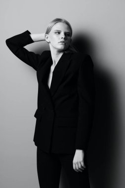 Klasik takım elbiseli çekici sarışın bir kız elleriyle saçlarını tutuyor ve stüdyoda siyah beyaz tarzda profesyonel bir model gibi poz veriyor. Moda fotoğrafçılığı. Kıyafet mağazaları için konsept. Yüksek kalite fotoğraf