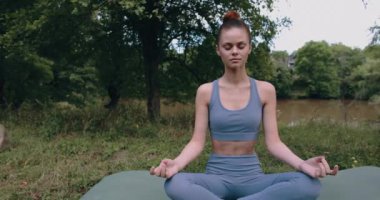 Nilüfer çiçeği pozunda meditasyon yapan bir kadın yazın yeşil çimenler üzerinde spor giyim parkında yoga yaparken. Yüksek kalite 4k görüntü