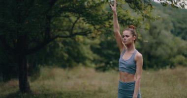 Parktaki bir kadın spor kıyafetleri içinde spor kıyafetleri ve doğa yaşam tarzıyla uyum içinde sırt ve bacak kaslarını esnetiyor ve pompalıyor. Yüksek kalite 4k görüntü