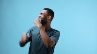Afro-Amerikalı adam mavi tişörtle neşeli bir müzikle dans ediyor. Stüdyo geçmişi mutlu ve özgür. Yüksek kalite 4k görüntü
