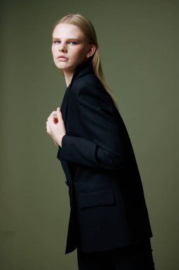 Sarışın güzel ceketini yakasından tutuyor. Stüdyoda yeşil bir arka planda yarım yamalak poz veriyor. Kıyafet markaları için konsept fotoğraf. Şık takımlar için harika bir teklif. Yüksek kalite fotoğraf