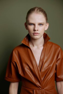 Mevsimlik indirim teklifi. Kendine güveni tam, deri ceketli genç bir bayan zeytin yeşili stüdyo arka planında izole edilmiş akşam makyajını gösteren mavi gözlü bir kadın.