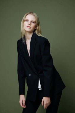 Siyah takım elbiseli göz kamaştırıcı zarif bir kız öne eğiliyor ve stüdyoda yeşil bir arka planda profesyonel pozlar veriyor. Markalar için reklam kavramı. Yüksek kalite fotoğraf