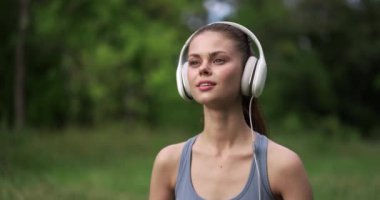Parktaki spor eğitiminden sonra çimenlerde dinlenen ve gülümseyen müzik dinleyen genç bir kadın. Yüksek kalite 4k görüntü