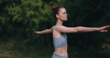 A woman warms up her body before a workout in nature. The concept of an athletic body and health. High quality 4k footage