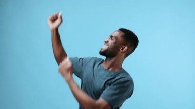 Afro-Amerikalı adam mavi tişörtle neşeli bir müzikle dans ediyor. Stüdyo geçmişi mutlu ve özgür. Yüksek kalite 4k görüntü