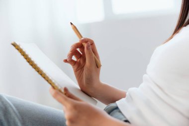 Genç esmer, elinde kalem ve defter tutarken yandan bakıyor. Yazar konsepti. Mekan Teklif Sancağını kopyala. Yakın çekim.