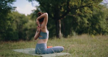 Genç bir kadın spor giyim kuşamında parkta spor yapıyor ve sırtını sıvazlıyor. Lastik bir bantla egzersiz yapmak. Yüksek kalite 4k görüntü