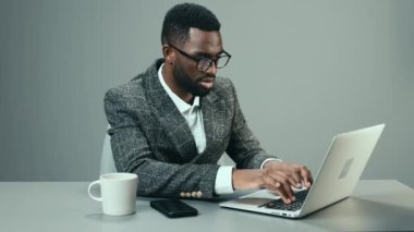 Ofiste çalışan Afro-Amerikalı bir işadamı masasında bir kupa kahveyle gri arka planda ve yorgun. Yüksek kalite 4k görüntü