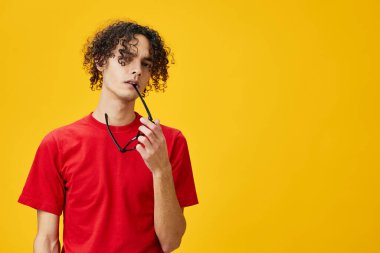 Kırmızı tişörtlü, miyop genç adam sarı stüdyo arka planında izole edilmiş diş poz verirken komik gözler tutuyor. Reklamcılık için bedava olan en iyi teklif. Eğitim Koleji konsepti
